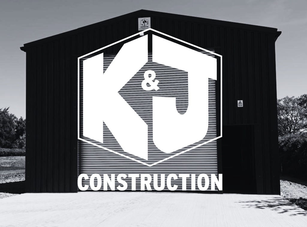 Black and white picture of a steel frame building with the K & J Construction logo layered over the top.